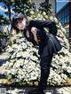 A woman in a black suit standing in front of a bunch of white flowers.