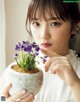 A woman holding a potted plant with purple flowers in it.