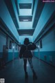 A woman walking down a long hallway holding a camera.