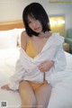 A woman in a white shirt and yellow panties sitting on a bed.