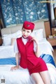 A woman in a red uniform sitting on a bed.